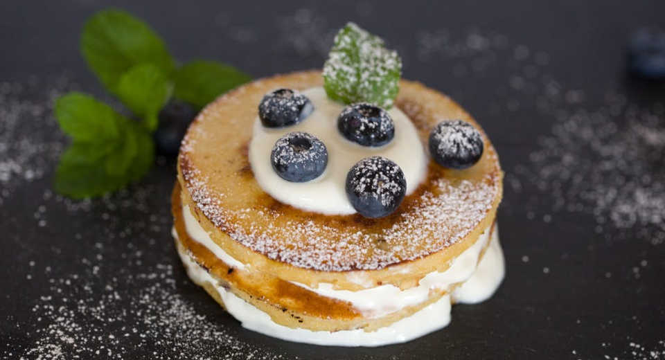 Romantisches Frühstück im Bett mit Pancakes, Blaubeeren und Creme