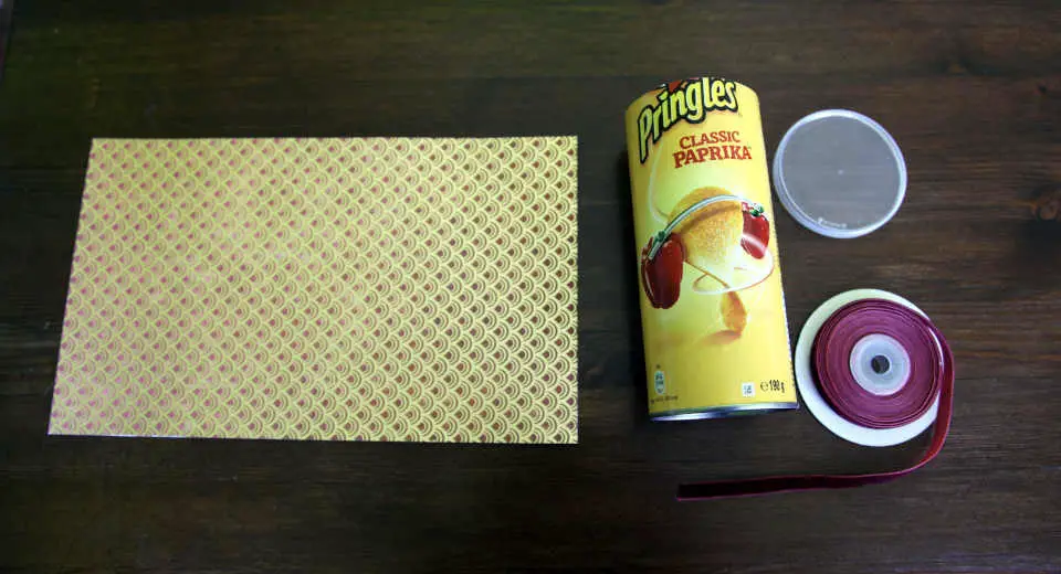Um eine runde Geschenkbox zu basteln aus einer Pringelsdose benötigt man schönen Motivkarton und Samtband.