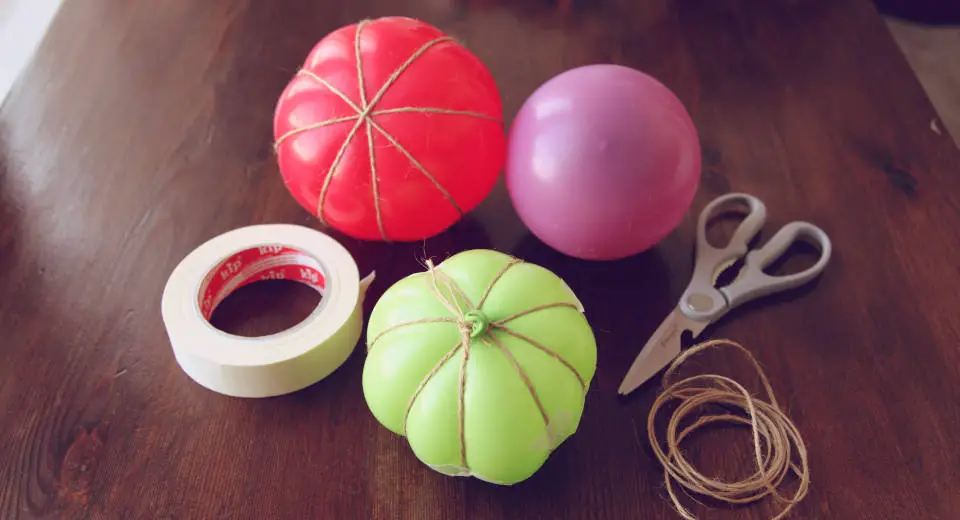 To make a paper mache pumpkin, you first need to wrap twine around the balloons and fix it with masking tape